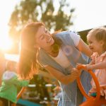 Mother play and smile with toddler girl at playground seesaw swi